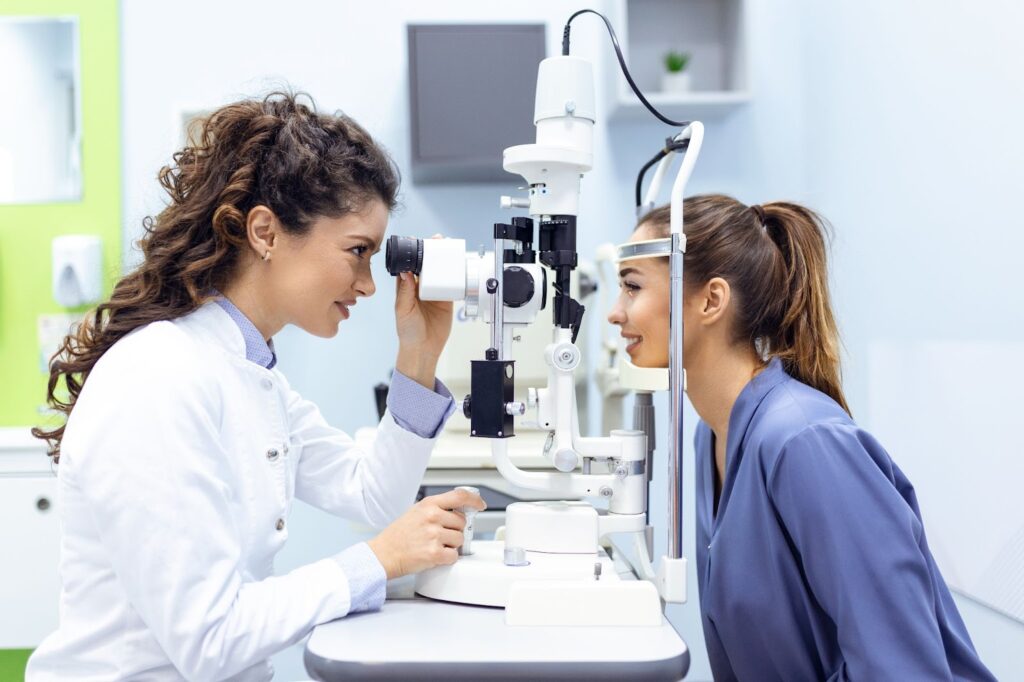 A female optometrist examining a young female patient's eyes while smiling.