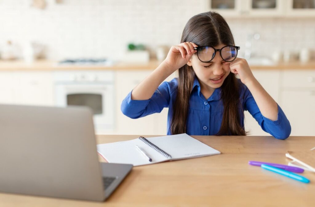 A girl lifts her glasses and rubs her eyes, indicating that she may have a refractive error like myopia at work.