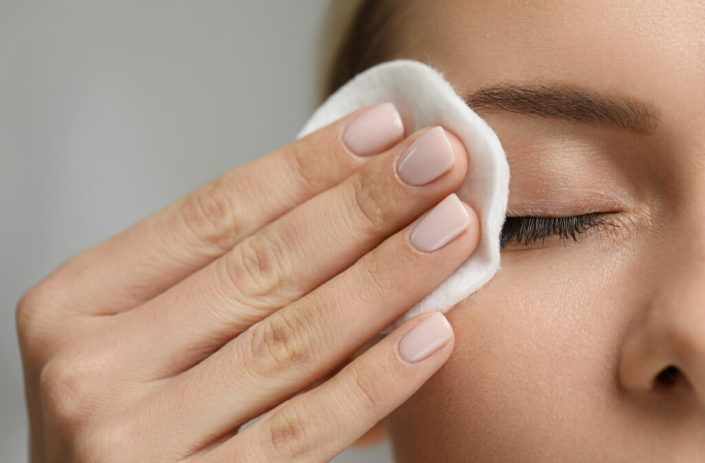 Close-up of a woman’s hand wiping her upper eyelid using a soft cotton pad to clean it as part of good eyelid hygiene