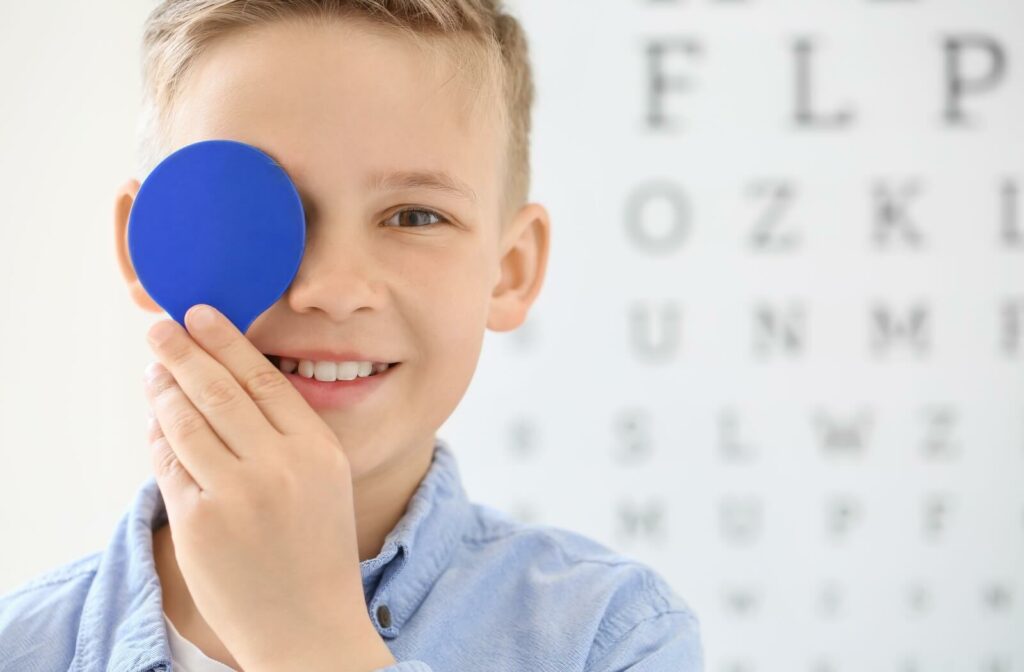 Smiling child holding a vision testing tool in front of one eye during an eye exam.
