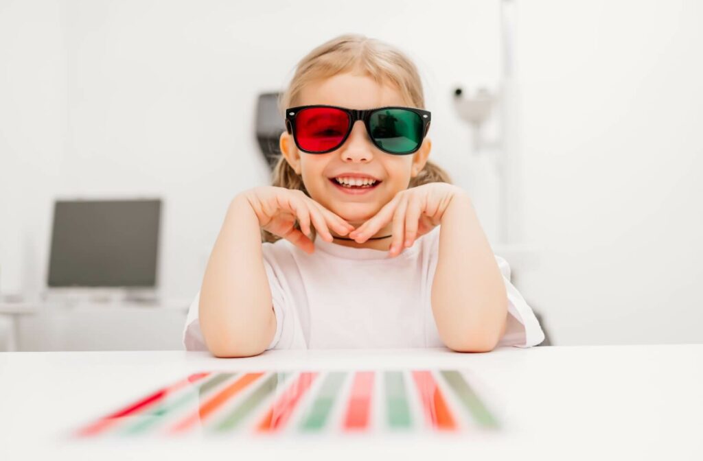 Young girl smiling during vision therapy session, wearing glasses with one red lens and one green lens.