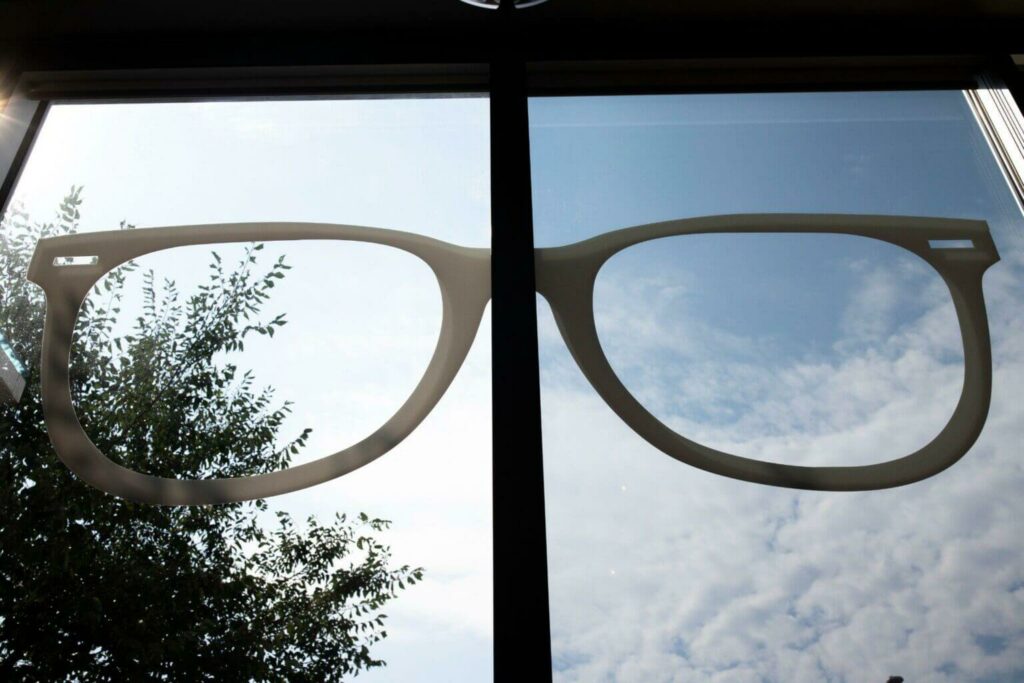Eyeglasses shown against a bright outdoor sky, with sunlight and clouds visible through the lenses.