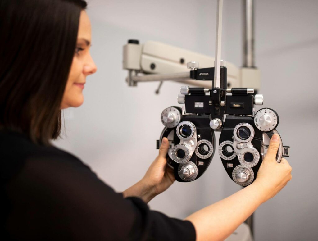 Eye care professional using a phoropter to measure a patient's vision prescription during an eye exam.