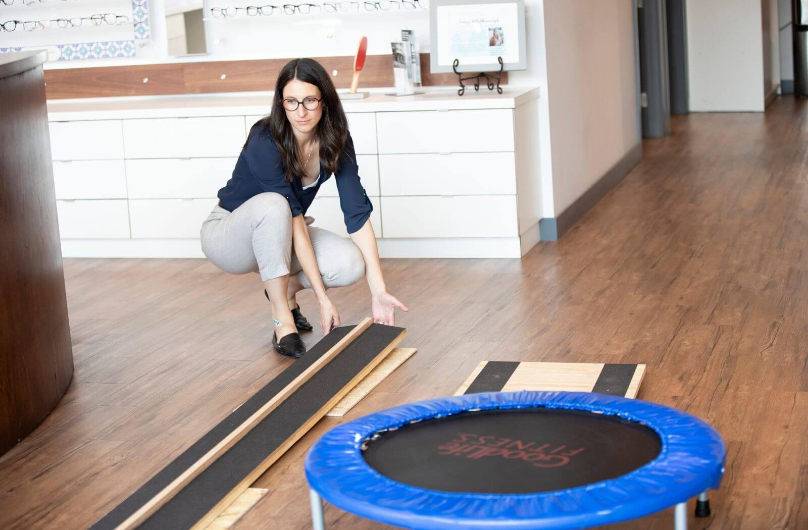 Woman setting up a visual coordination activity with balance boards and a small trampoline in an optical store.